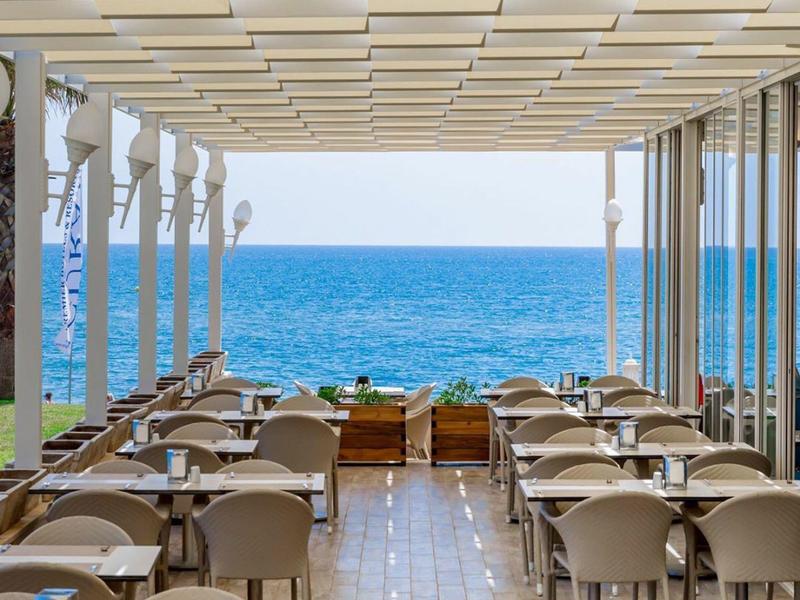 Outdoor restaurant with modern seating facing a clear blue sea under a white pergola.