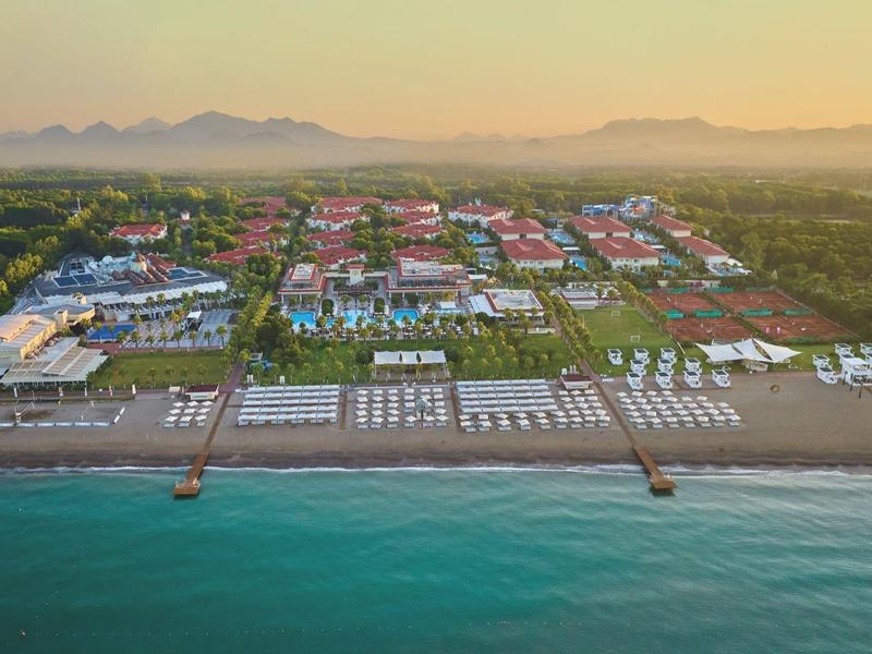A beachfront resort with pools, sun loungers, and villas near turquoise ocean water at sunset.