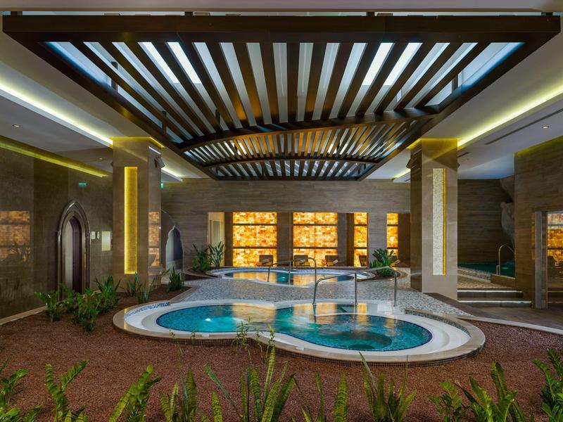Indoor spa pool with warm lighting and wooden ceiling beams in a luxury hotel.