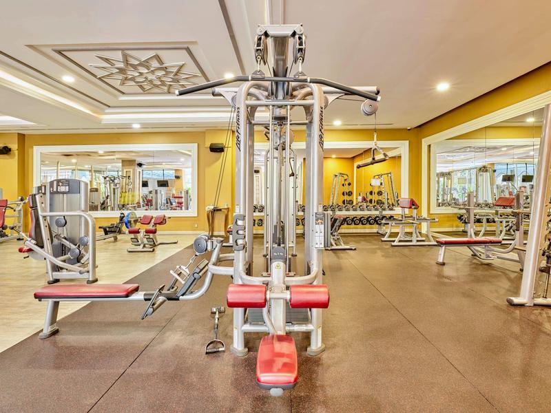 Spacious hotel gym with various exercise machines, weights, and mirrored walls in warm lighting.