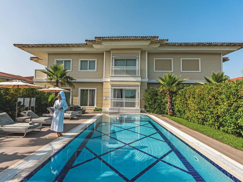 Modern house with large pool and terrace, surrounded by green garden.