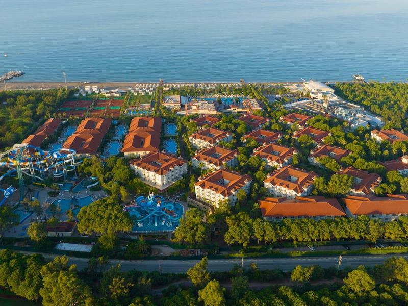 Resort with red-roofed buildings, green trees, and a blue pool near a coastal area.
