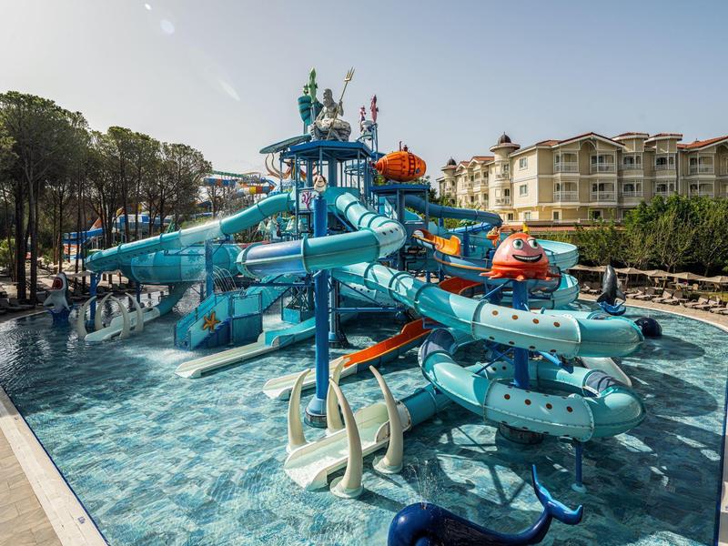 Multiple blue water slides in a pool with a hotel in the background.