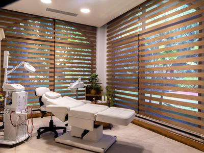 Sala trattamento moderna con lettino cosmetico, lampade e ampie persiane in legno.