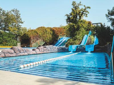 Area piscina blu con scivoli d'acqua circondata da alberi e rocce.