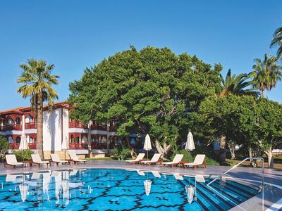 Grande piscina davanti all'hotel con lettini e alberi verdi sullo sfondo