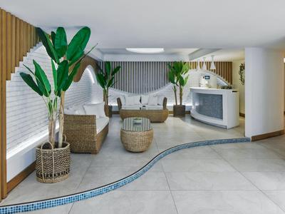 Luminosa hall d'hotel con mobili in rattan moderno, piante e motivo di piastrelle curva sul pavimento.