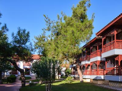 Edifici dell'hotel con balconi rossi circondati da alberi verdi e prato sotto un cielo azzurro.