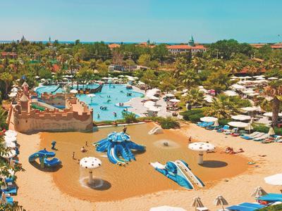 Großer Wasserpark mit mehreren Pools, Wasserrutschen und Sonnenschirmen in einer Hotelanlage.