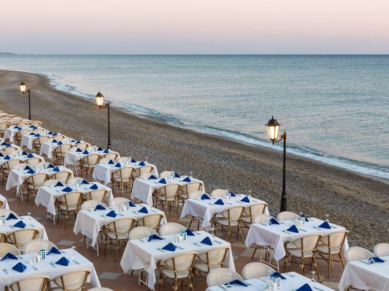 Ristoranti sulla spiaggia con tavoli apparecchiati e sedie vicino al mare sotto i lampioni.