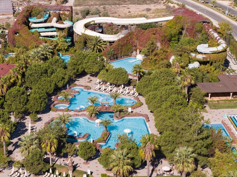 Vista di un'area piscina dell'hotel con più piscine, scivoli d'acqua e molta vegetazione.