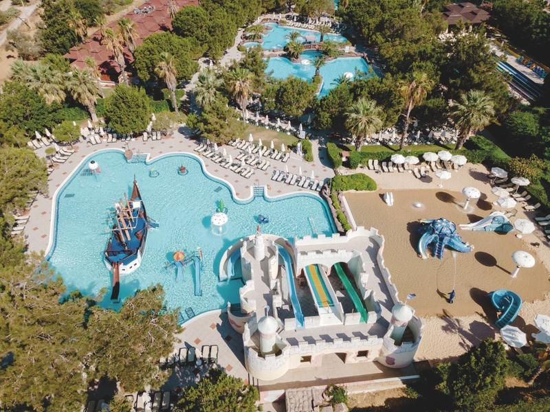 Grande piscina dell'hotel con scivoli d'acqua e aree giochi, circondata da lettini e alberi.