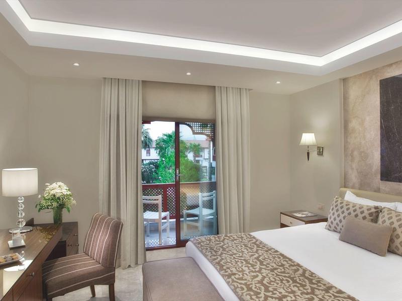 Camera d'hotel elegante con letto grande, poltrona, scrivania e balcone con vista sul verde.