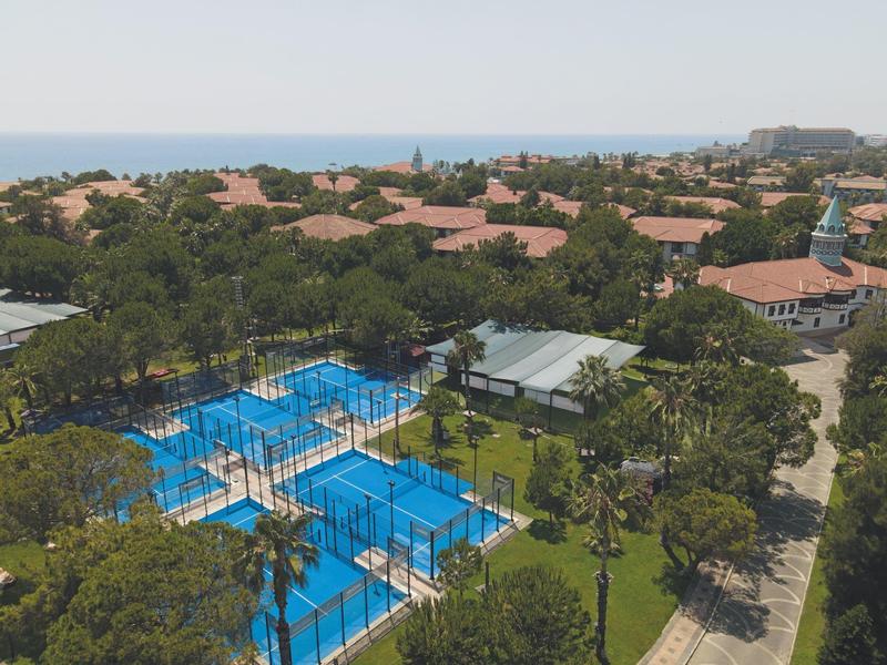 Vista di un resort con più piscine, palme e edifici con tetti rossi vicino al mare.