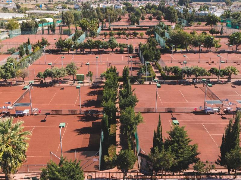 Vista aerea di campi da tennis in terra rossa circondati da vegetazione in un'area alberghiera.