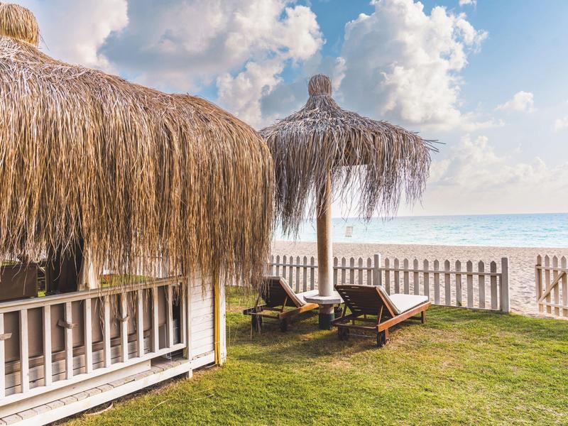 Vista sulla spiaggia con capanna di paglia e lettini su prato verde di fronte al mare e al cielo