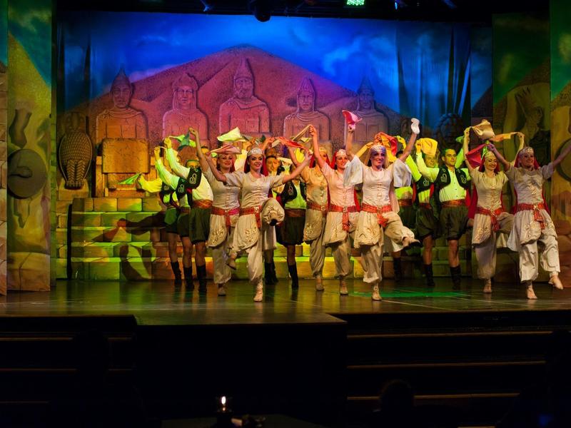 Gruppo di ballerini in costumi colorati che si esibisce su un palco con sfondo vivace.