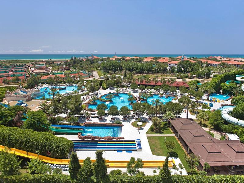 Grande villaggio turistico con diverse piscine, scivoli d'acqua e aree verdi sotto un cielo limpido.