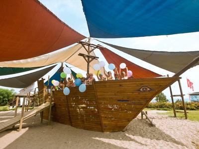 Duży drewniany statek na piasku z kolorowymi balonami i materiałami do cienia.