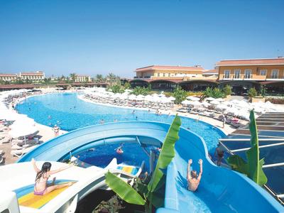 Großer Swimmingpool mit Wasserrutsche und vielen Liegestühlen unter klarem blauem Himmel