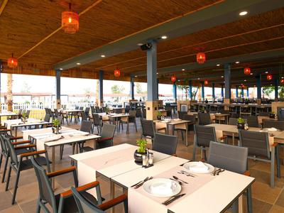 Przestronna nowoczesna restauracja z nakrytymi stołami i pośrednim oświetleniem pod drewnianym sufitem.