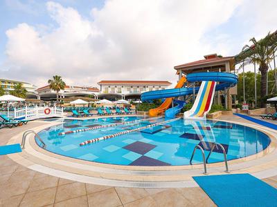 Basen hotelowy z kolorowymi zjeżdżalniami i leżakami pod pochmurnym niebem.