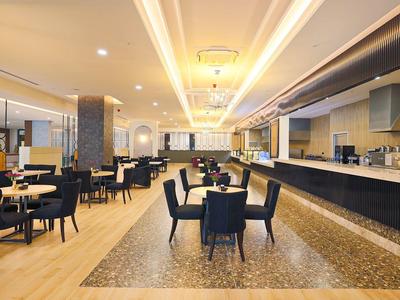 Nowoczesna restauracja hotelowa z czarnymi krzesłami, drewnianą podłogą i długim barem.