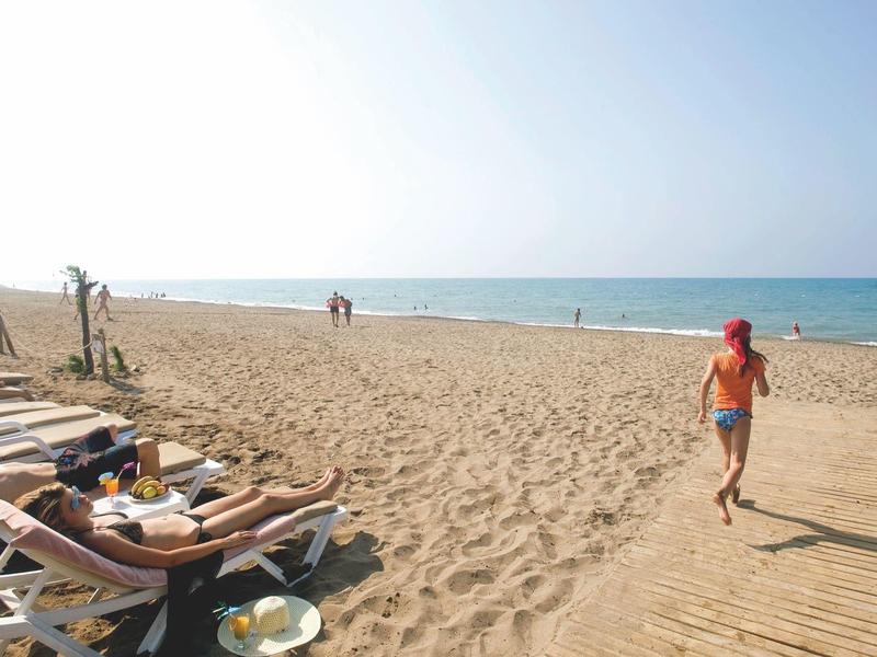 Szeroka piaszczysta plaża z leżakami i osobą idącą w stronę morza.