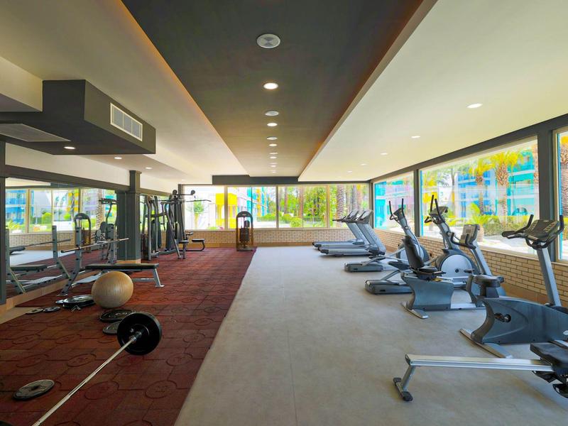 Nowoczesna siłownia z różnymi urządzeniami treningowymi i widokiem na teren na zewnątrz.