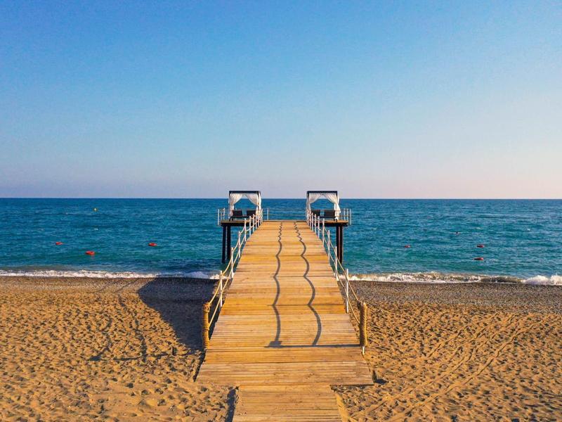 Piaszczysta plaża z drewnianym pomostem i schodami prowadzącymi prosto do spokojnego niebieskiego morza.