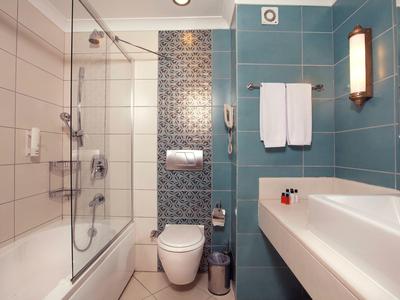 Modernes Badezimmer mit blauen Fliesen, Badewanne, Glasduschwand, WC und Waschbecken mit Handtüchern.