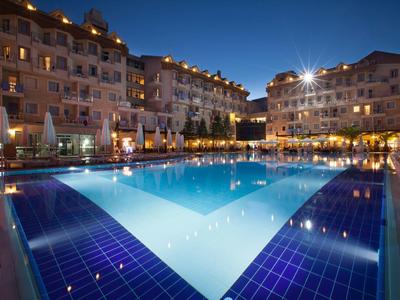 Beleuchteter Pool mit blau-lila Fliesen, umgeben von mehrstöckigen Hotels bei Nacht.