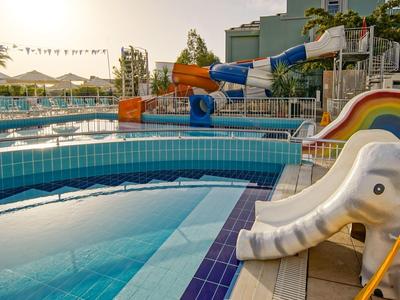 Ein leeres Schwimmbecken mit einer weißen Elefantenrutsche und bunten Wasserrutschen im Hintergrund.