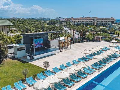 Grande piscina all'aperto con lettini e area palco in resort tropicale sotto il sole.