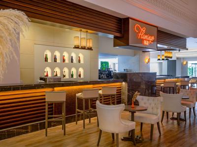 Nowoczesny bar hotelowy z drewnianym kontuarem, białymi krzesłami i dekoracjami w ciepłym świetle.