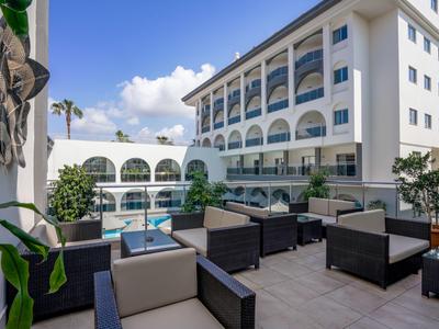 Nowoczesny taras hotelowy z miejscami do siedzenia i widokiem na basen oraz budynek hotelu w świetle dziennym.