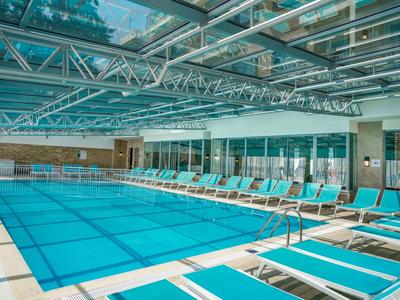 Nowoczesny basen kryty z przeszklonym dachem i leżakami wzdłuż basenu.