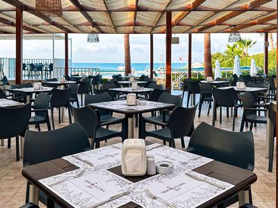 Restauracja z ciemnymi krzesłami i stolikami na zadaszonym tarasie z widokiem na morze.