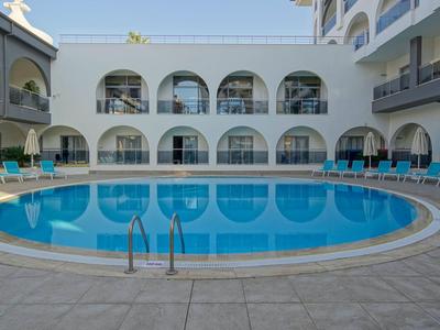 Okrągły basen na dziedzińcu hotelu z niebieskimi leżakami i białymi ścianami.