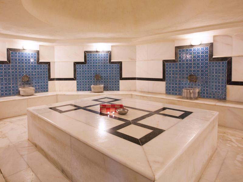 Stanza di hammam rotonda e luminosa con piastrelle blu e un grande tavolo in marmo al centro.