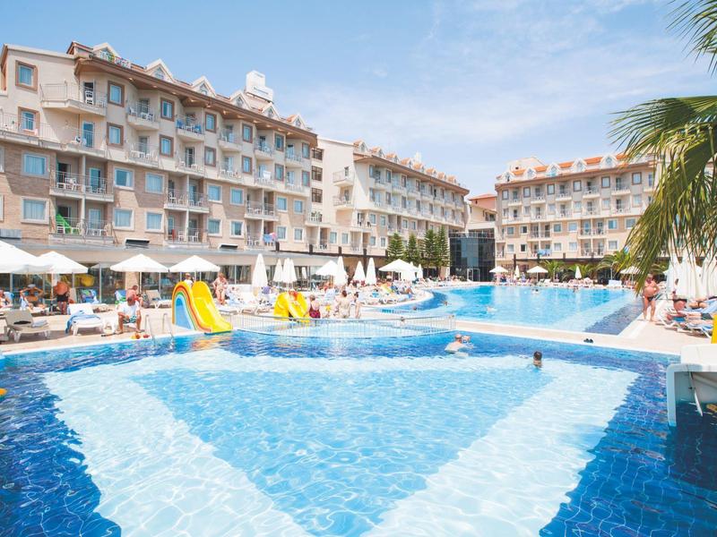 Grande piscina dell'hotel con ombrelloni, lettini e scivoli davanti a edifici pluripiano.