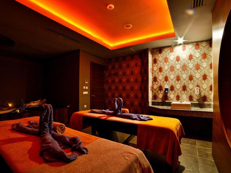 Accogliente sala spa con due lettini da massaggio, illuminazione calda e sculture di asciugamani decorative.