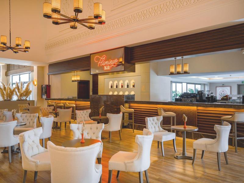 Elegante bar dell’hotel con poltrone bianche moderne, tavoli in legno e ambiente illuminato caldo.