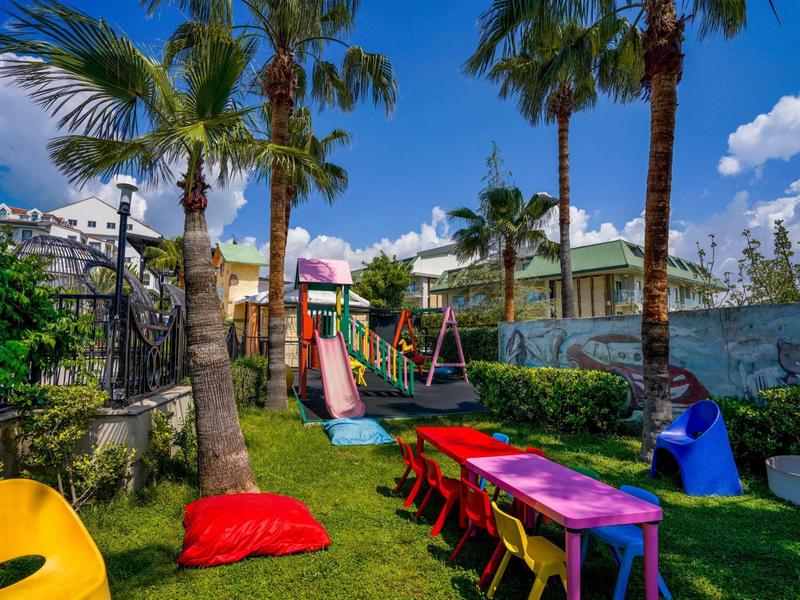 Parco giochi per bambini con tavoli e sedie colorate sotto palme nel giardino dell'hotel