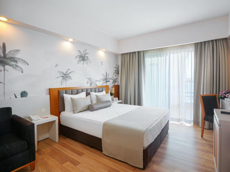 Camera d'hotel moderna con letto matrimoniale, balcone e scrivania in un'atmosfera luminosa e accogliente.