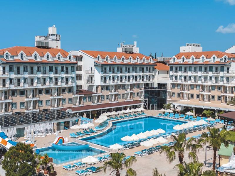 Grande hotel su più piani con piscina centrale sotto un cielo azzurro.
