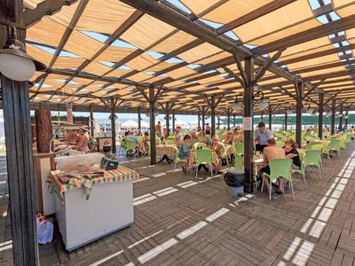 Terrazza coperta con ospiti seduti su sedie verdi sotto una tenda da sole.