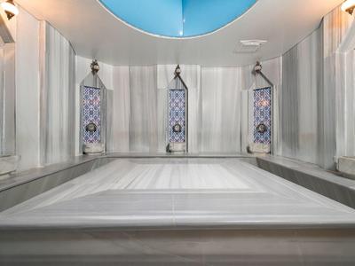 Bagno turco moderno con vasca in marmo e piastrelle decorative sotto un'apertura circolare nel soffitto.