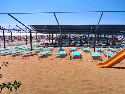 Spiaggia con ombrelloni, lettini e un'area giochi per bambini con scivolo sulla sabbia.