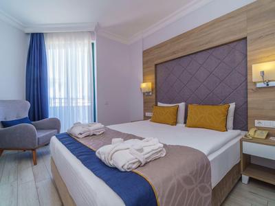 Chambre d'hôtel confortable avec lit double, deux peignoirs et fauteuil près de la fenêtre.